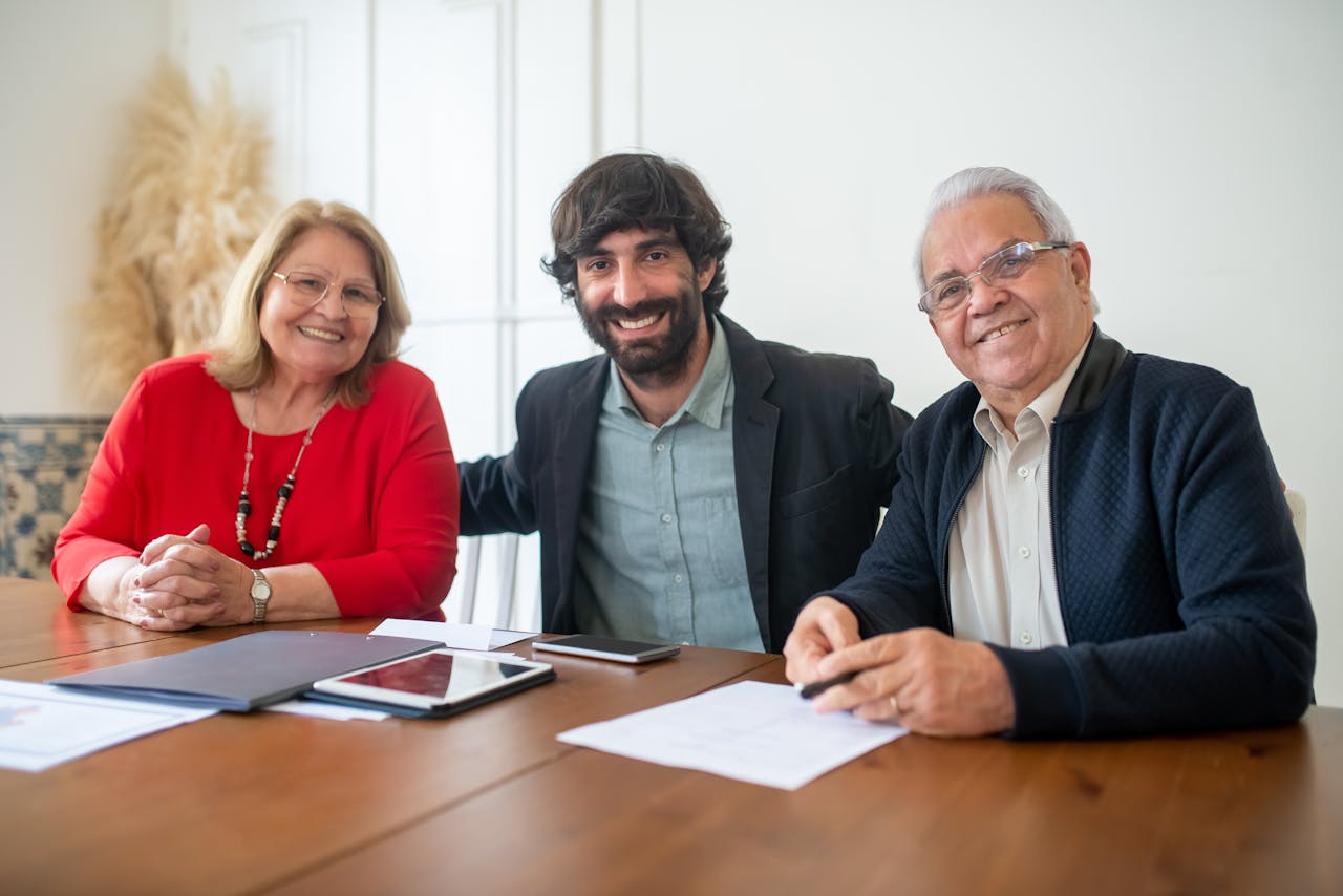 Group portrait of two senior adults and a young man smiling at a business meeting indoors.