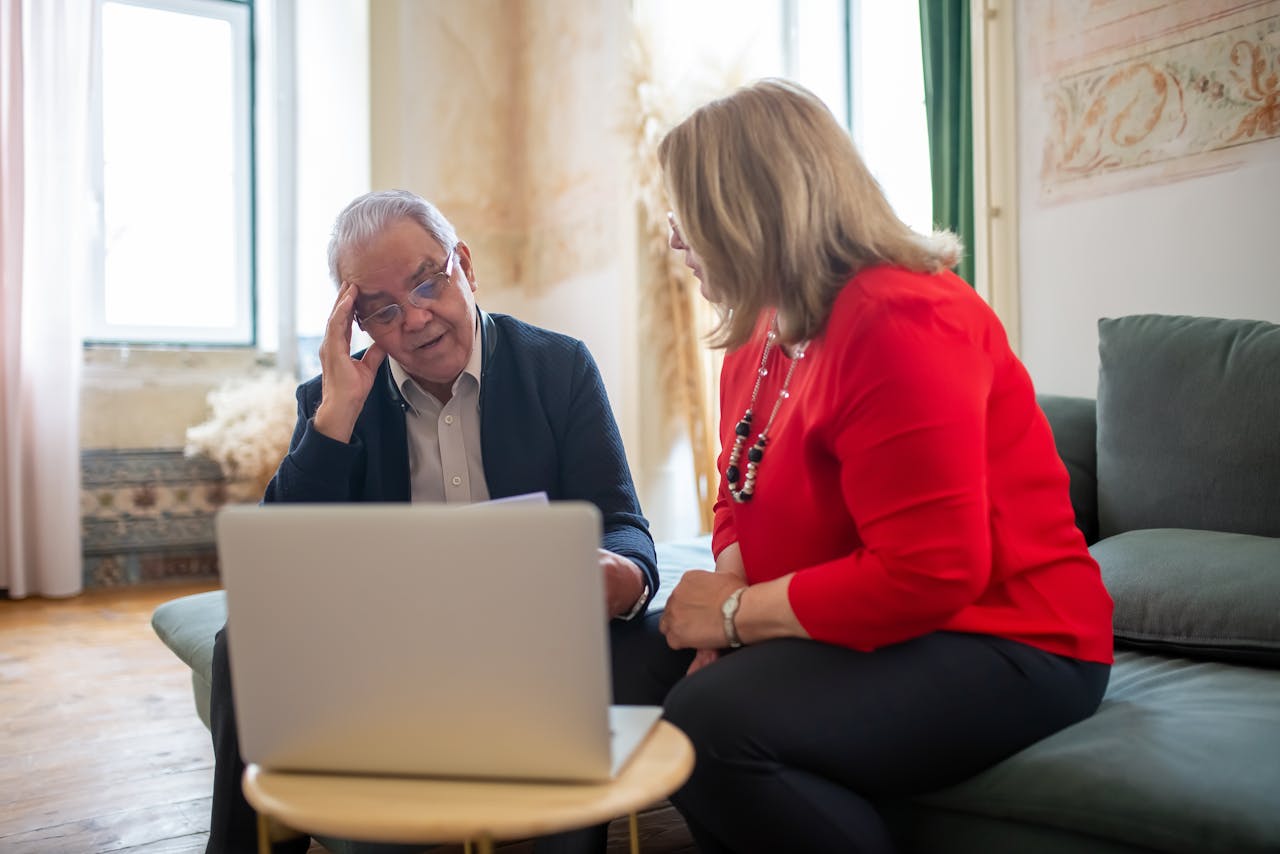 Elderly couple contemplating and talking over a laptop in a cozy indoor setting.